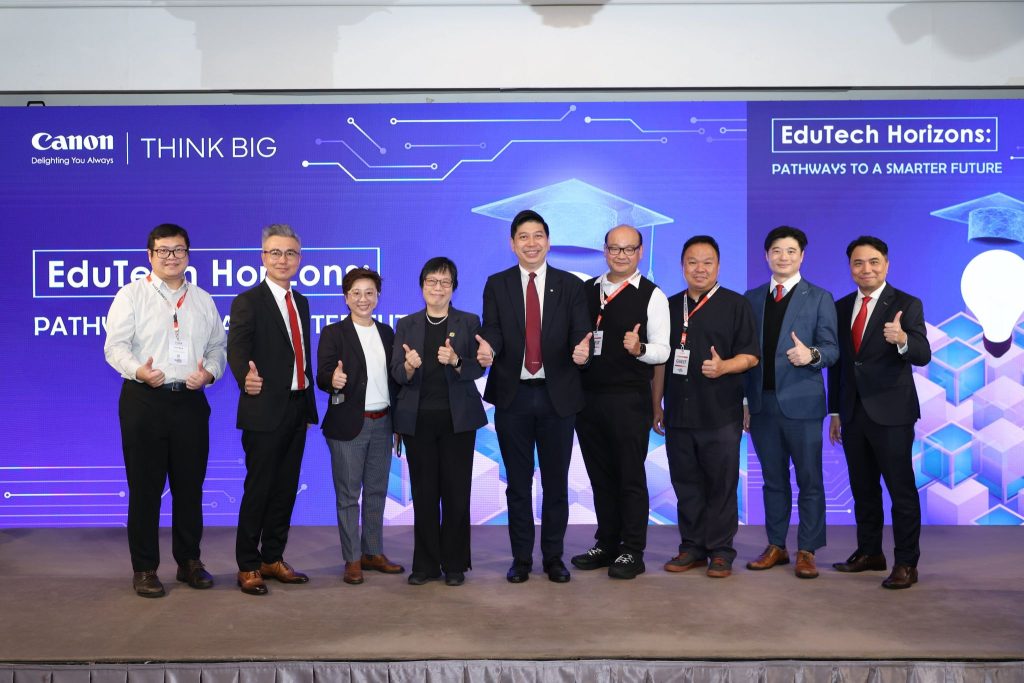 Eight people in business attire stand on a stage in front of a blue "EduTech Horizons: Pathways to a Smarter Future" backdrop, smiling and giving thumbs up at a professional event.