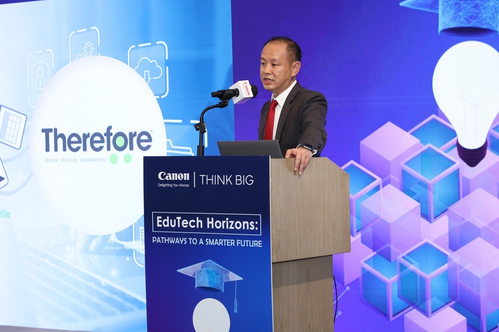 A man in a suit speaks at a podium during the "EduTech Horizons: Pathways to a Smarter Future" event, with "Canon" and "Therefore" logos and digital graphics displayed on screens behind him.