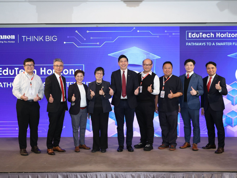 Nine people in professional attire stand in a row on stage, smiling and giving thumbs up, in front of a blue event backdrop with the “Canon” logo and the event name, ThinkBIG “EduTech Horizons: Pathways to a Smarter Future" with technology-themed graphics.